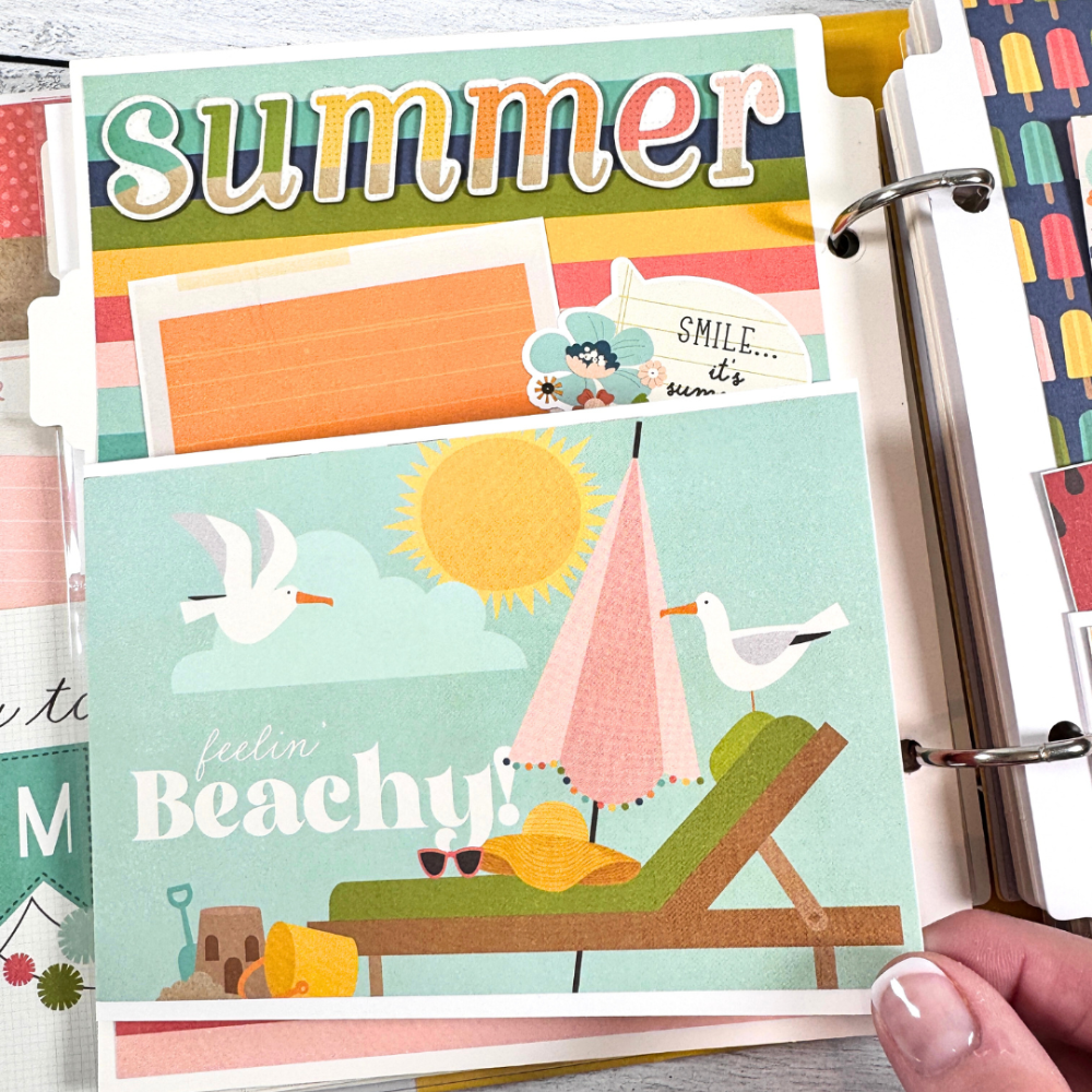Sunny Days Summer Scrapbook Album Page with a folding card, rainbow stripes, a beach chair, an umbrella, the sun, seagulls, and a sand castle